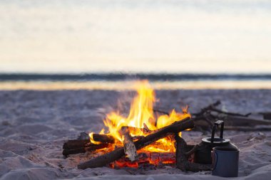 Dalgalar günbatımı sırasında yanındaki sahil kamp ateşi yanıklar. Deniz kenarına harika seyahat.