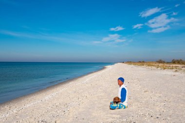 Gezgin komik köpek ile turkuaz denizin yanında ıssız sahilde güneşli bir günde oturur ve derin derin düşünür. Deniz kıyısı harika macera seyahat. Geniş açı.