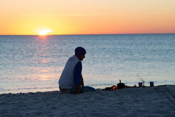 海岸で焚き火の隣に旅行者の座っている瞑想し 海の向こうの夕日を賞賛します 海辺への素晴らしい旅行 — ストック写真