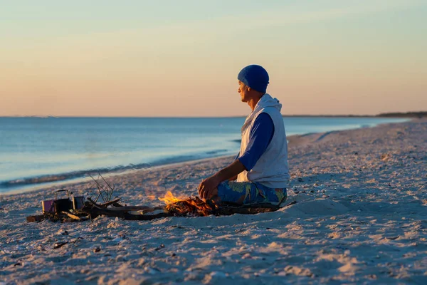 海岸で焚き火の隣に旅行者の座っている瞑想し 海の向こうの夕日を賞賛します 海辺への素晴らしい旅行 — ストック写真