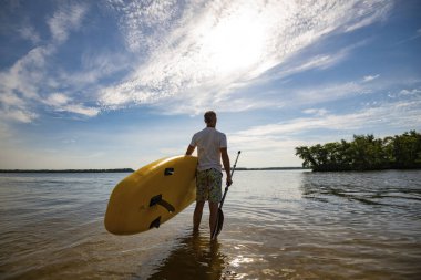 Mutlu bir adam büyük bir Nehri üzerinde bir Sup kurulu ile güneşli gün duruyor. Yukarı raket yatılı - stand doğada awesome Aktif istirahat. Geniş açı, arkadan görünüm.