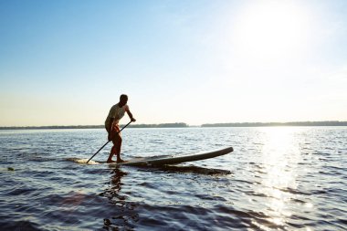 Büyük bir nehir üstünde a Sup tahta kürek çekmeye neşeli adam. Yukarı raket yatılı - stand harika etkin açık rekreasyon ve eğitim.
