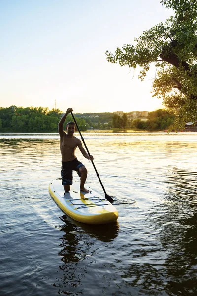 Joyful multiracial guy paddling on a SUP board having fun and looking to the camera. Stand up paddle boarding - awesome active outdoor recreation.