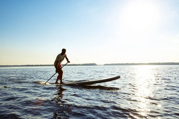 Joyful  guy paddling on a SUP board on a big river. Stand up paddle boarding - awesome active outdoor recreation and training.