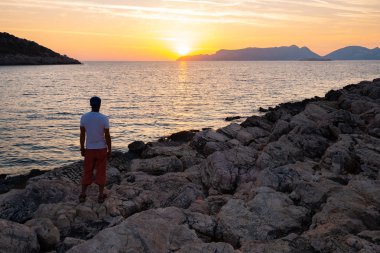 Gezgin rock sahil üzerinde duruyor ve muhteşem günbatımı - macera seyahat boyunca Likya yolu, Türkiye'nin hayran. Arkadan görünüm.