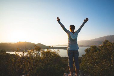 Mutlu traveler, kadın kollarını açarak kayanın üzerinde duruyor ve Akdeniz'in turkuaz suları günbatımı - Likya yolu, Türkiye'nin boyunca macera seyahat sırasında hayran. Arkadan görünüm, arkadan.