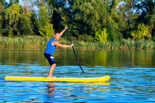 Happy man is training on a SUP board on large river and enjoying life. Stand up paddle boarding - awesome active outdoor recreation.