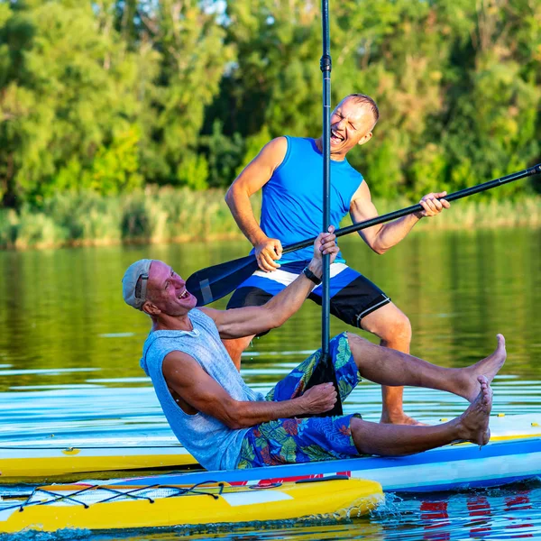 Joyful friends, a SUP surfers relax on the big river during sunset and having fun. Stand up paddle boarding - awesome active outdoor recreation.