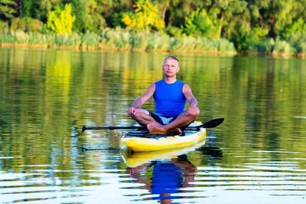 Man is relaxing and meditating on a SUP board on large river and enjoying life. Stand up paddle boarding - awesome active outdoor recreation.