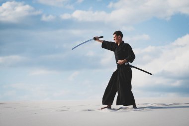 Adam kılıç katana ile geleneksel Japon elbiseleri günbatımı - samuray bulutlu gökyüzü arka plan üzerinde eğitim dövüş sanatları çölde sırasındadır.