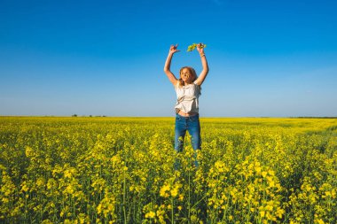 Kollarını açarak, mavi gökyüzü altında sarı çiçek alan üzerinde atlar neşeli güzel kadın sarışın hayat sahiptir ve eğlence - mutluluk ve özgürlük doğada var.