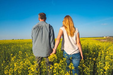 Romantik Çift sarı çiçek mavi gökyüzünün altında alan aracılığıyla güneşli akşam - mutluluk ve özgürlük doğada yürüyüş mesafesindedir. Arkadan Görünüm.