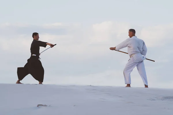 和服の二人の男は日本の伝統的な武器 刀とチョ 夕暮れ砂漠で格闘技を練習しています — ストック写真