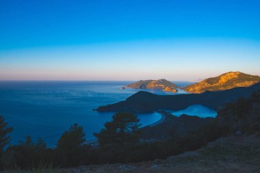 Panoramik manzaralı kayalık sahilleri sunrise - Ölüdeniz, Türkiye'de turist Simgesel Yapı sırasında Akdeniz'in turkuaz suları ile çevrili yemyeşil çam ağaçları ile kaplı.