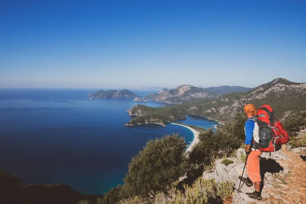 Traveler with backpack stands on the cliff and admires the amazing sea bay at sunny day - awesome adventure travel in Turkey. Back view, wide angle.