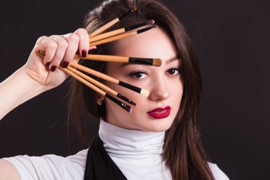 Elinde fırçayla siyah arka planda makyaj sanatçısı.