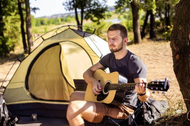 Adam gitar müzik çadırın yakınında t katlanır sandalye üzerinde çalış