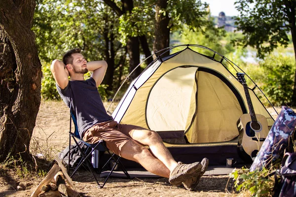 Een man rust in de buurt van een tent op een klapstoel in het bos. — Stockfoto