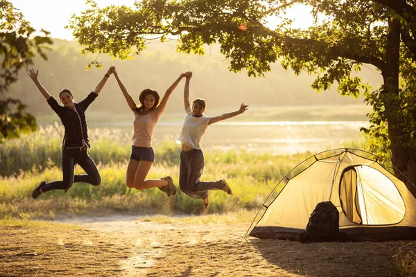 Drie vrienden springen bij zonsondergang in de buurt van de tent. Groep toeristen op — Stockfoto
