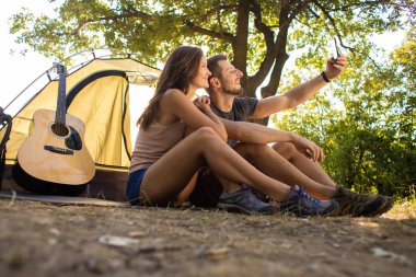 Kamp yapan bir adam ve bir kadın çadırın yanında selfie çekiyorlar..
