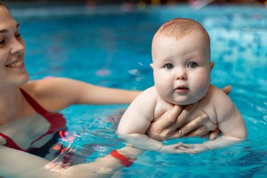 Anneyle bebek havuzda yüzmeyi öğreniyor.