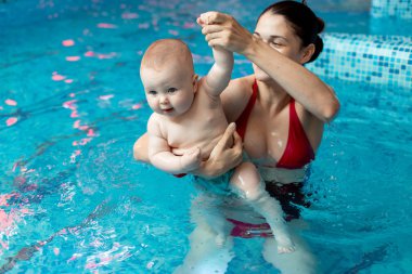 Anneyle bebek havuzda yüzmeyi öğreniyor.