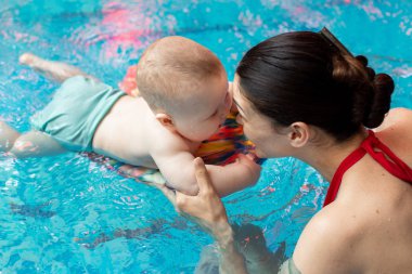 Anneyle bebek havuzda yüzmeyi öğreniyor.