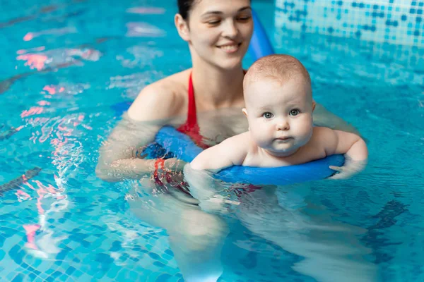 Anneyle bebek havuzda yüzmeyi öğreniyor.