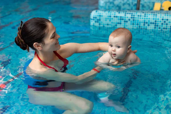 Anneyle bebek havuzda yüzmeyi öğreniyor.