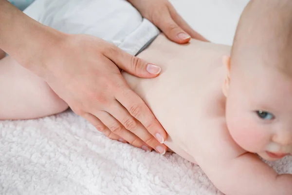 As mãos da mãe massageiam os músculos das costas de seu bebê . — Fotografia de Stock