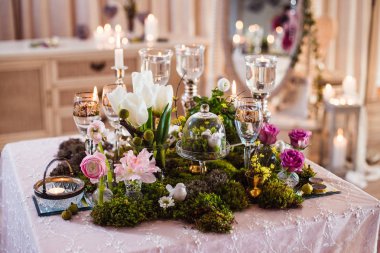 İki masa. Bastırılmış ışıkta romantik atmosfer, ışıklı mumlar ve rustik dekorasyon (orman yosunu, çiçekler, gözlükler ve vazolar)