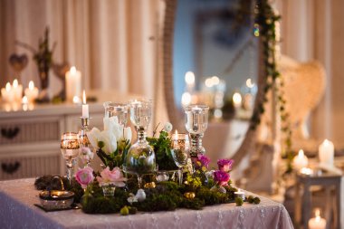 İki masa. Bastırılmış ışıkta romantik atmosfer, ışıklı mumlar ve rustik dekorasyon (orman yosunu, çiçekler, gözlükler ve vazolar)