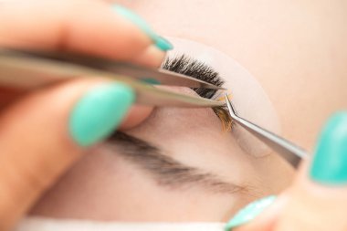 Efendi müşteriye büyük renkli kirpikleri biriktirir. Güzellik fotoğrafçılığına hazırlık. Bir resim oluşturuluyor.