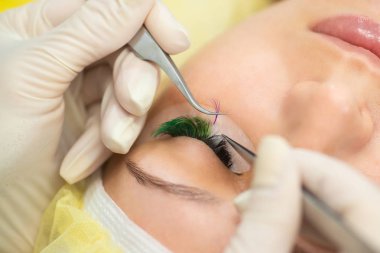 Efendi müşteriye büyük renkli kirpikleri biriktirir. Güzellik fotoğrafçılığına hazırlık. Bir resim oluşturuluyor.