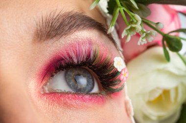 Güzel bir esmerin portresi. Kocaman kirpikleri var. Beyaz bir arkaplanda gül çelengi var..