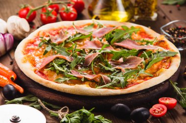 Etrafında malzemelerle koyu ahşap bir arka plan üzerinde pastırma ve arugula ile Pizza (yakın).