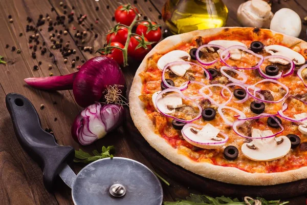 Italian pizza with mushrooms, olives and onion rings with ingredients on wooden table (close)