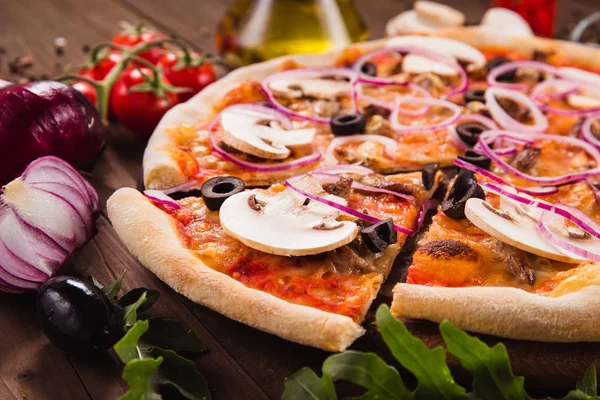 Italian pizza with mushrooms, olives and onion rings with ingredients on wooden table (close). Cut one piece