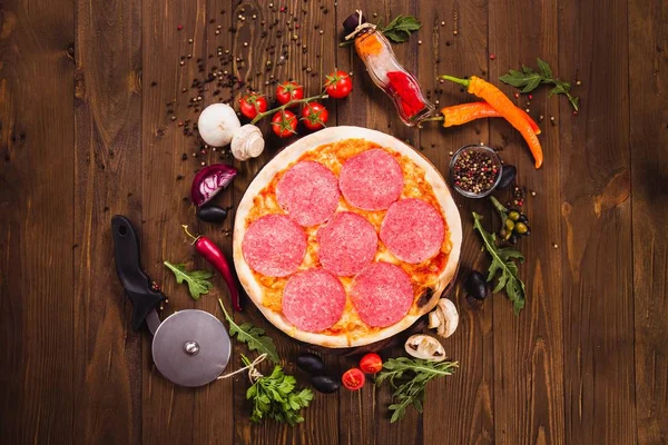 Etrafında malzemelerle koyu ahşap arka plan üzerinde salam dilimleri ile İtalyan pizza Pepperoni (yakın üst görünümü)