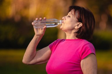Yaşlı kadın Gün batımında bir şişeden su içmek