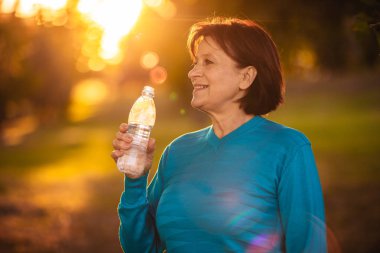 Yaşlı kadın Gün batımında bir şişeden su içmek
