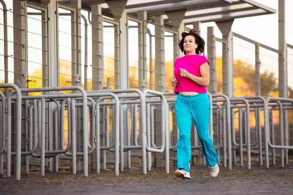 An elderly woman goes in for sports at sunset.