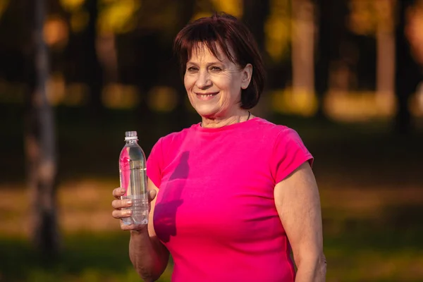Mujer mayor Beber agua de una botella al atardecer —  Fotos de Stock