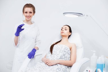 Doktor kozmetolojiuzmanı hastanın yüzünü enjekte ediyor