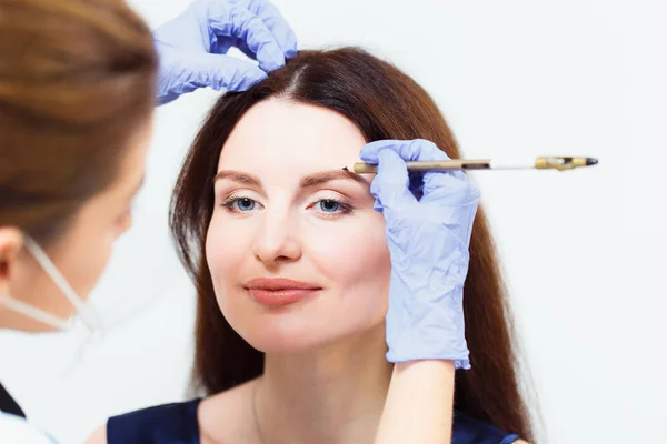 Make-up artist paints eyebrow pencil to beautiful brunette in be