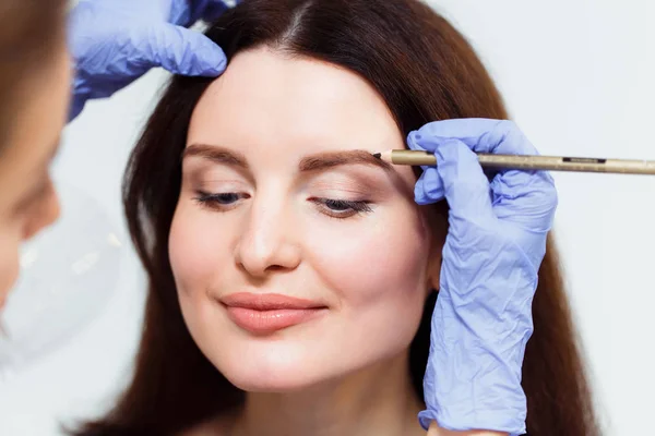 Make-up artist paints eyebrow pencil to beautiful brunette in be