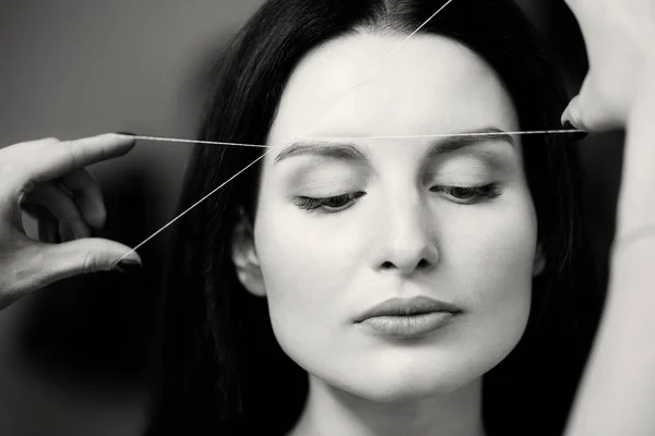 Cosmetologist plucks client eyebrows by thread — Stock Photo, Image