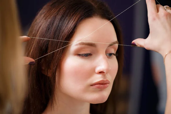 Cosmetologist plucks client eyebrows by thread — Stock Photo, Image