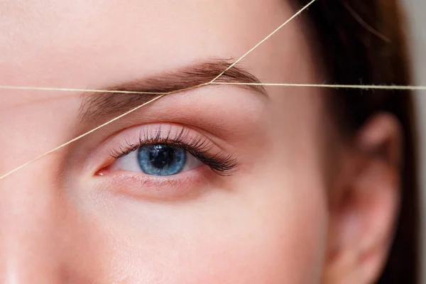 Cosmetologist plucks client eyebrows by thread. Close up