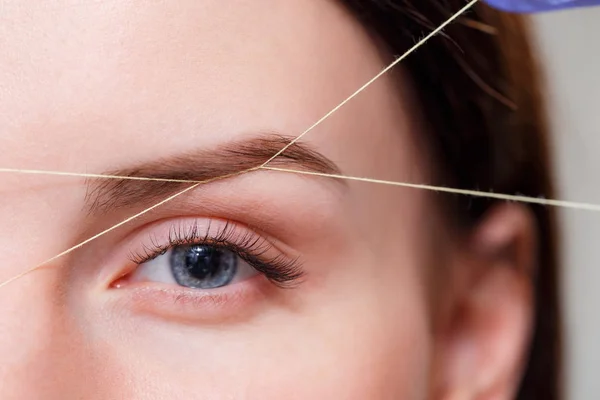 Cosmetologist plucks client eyebrows by thread — Stock Photo, Image